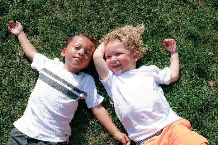 Двое детей лежат на траве на детской площадке