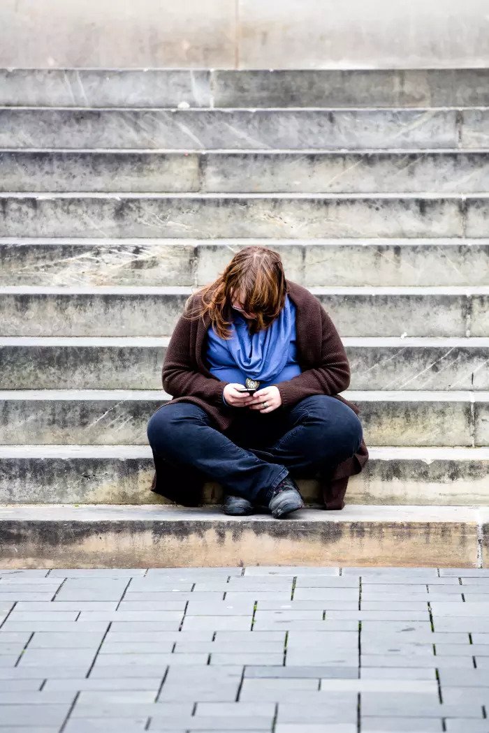 Толстая женщина сидит на лестнице и смотрит на смартфон