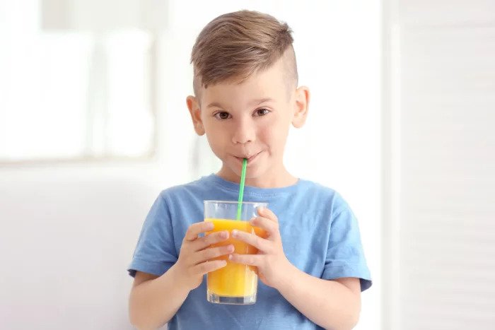 Мальчик пьет апельсиновый сок в соломе