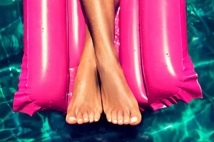 Загорелые ноги и окрашенные в черный цвет на фоне морского матраса и бассейна