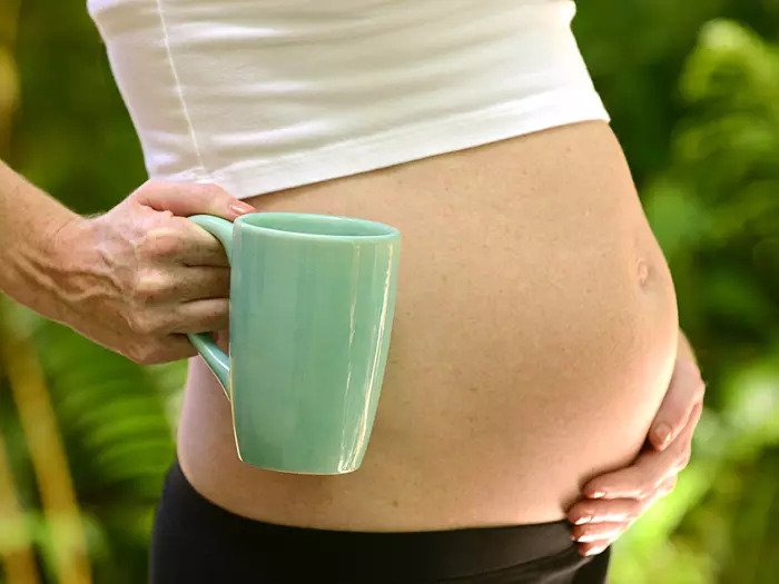 Беременная женщина держит чашку кофе