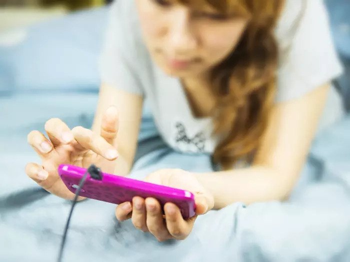 Женщина лежит на кровати с помощью смартфона