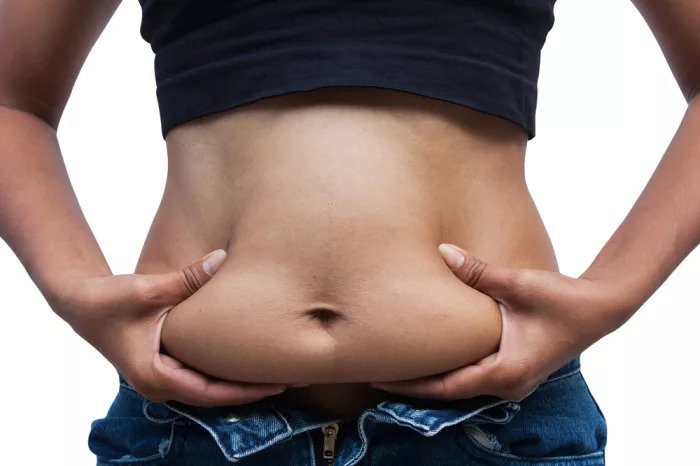 Женщина пытается закрыть джинсы на толстом животе
