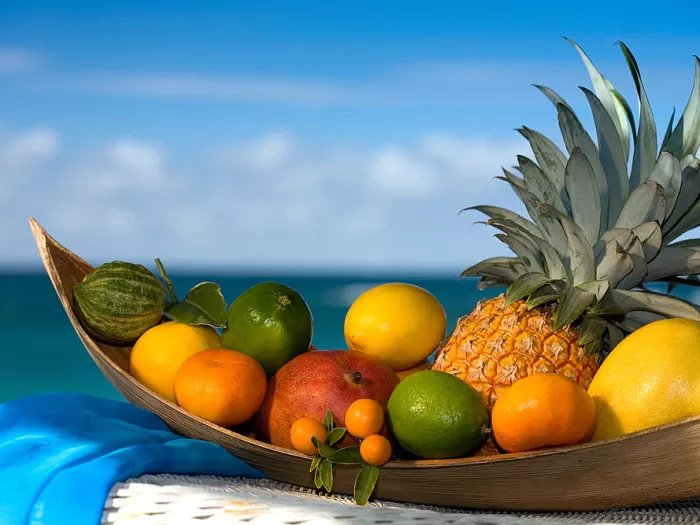 Тропические фрукты в деревянной тарелке в форме лодки на фоне воды